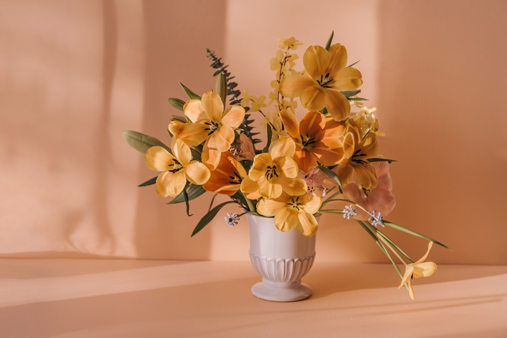 a white vase filled with yellow flowers on top of a table