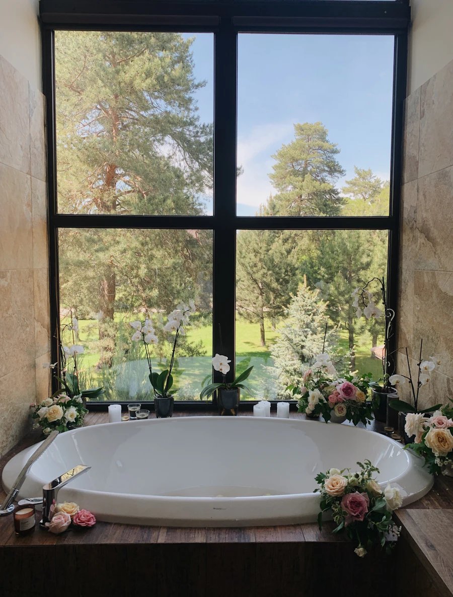 A deep bathtub beneath a tall window looking into pine trees