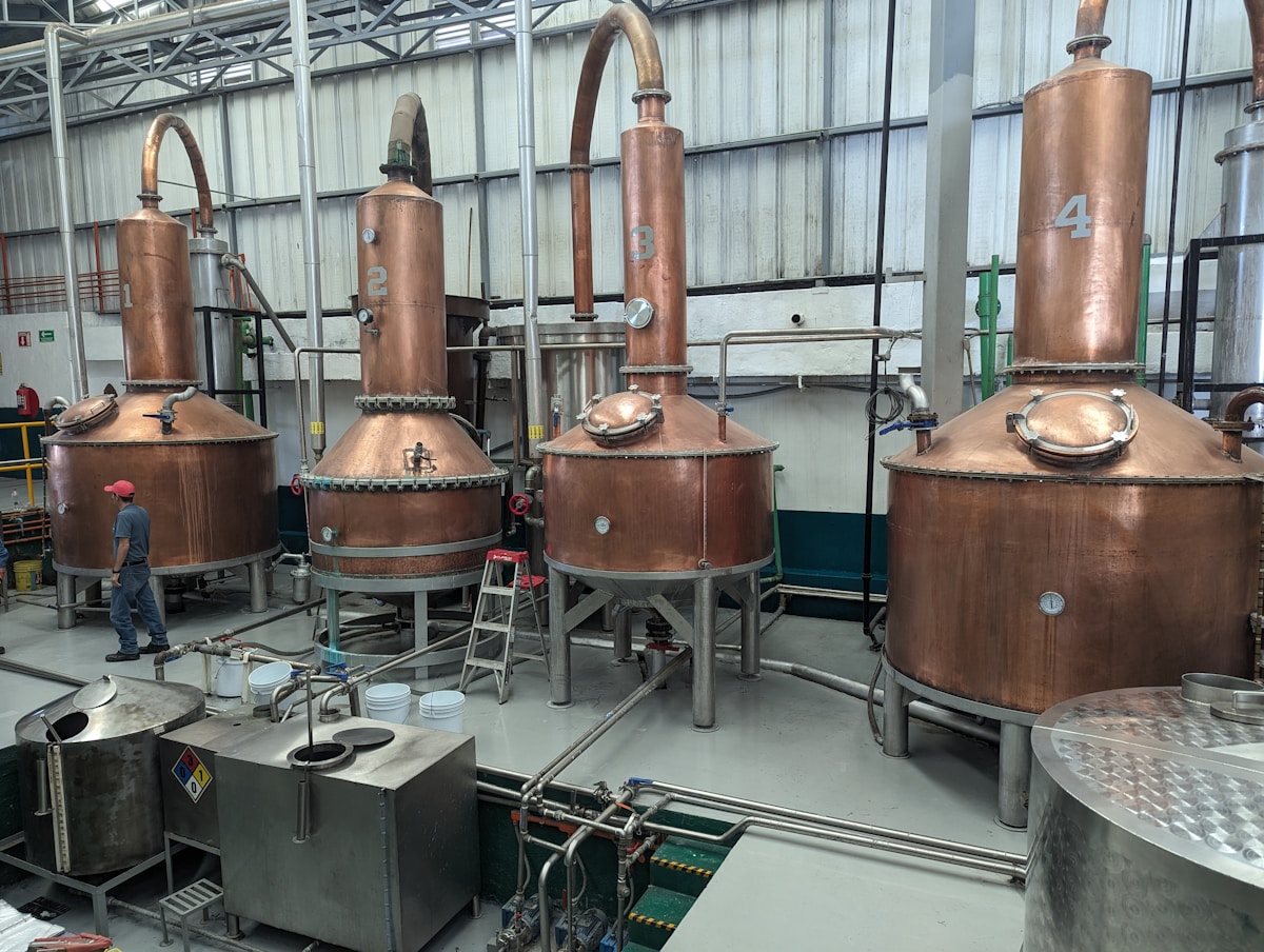 Copper pot stills inside a tequila distillery in Jalisco, Mexico, with a worker walking past for scale