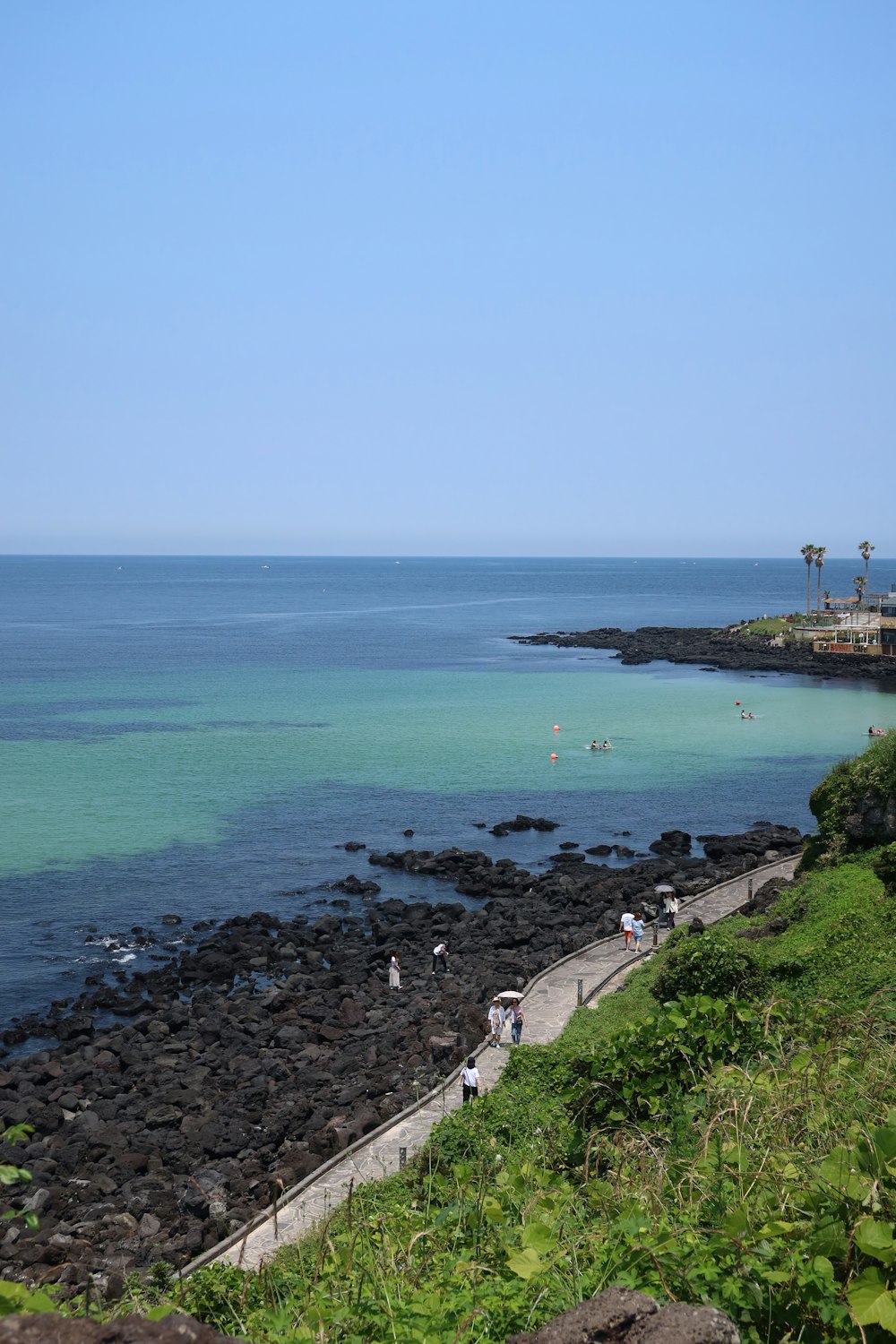 a group of people walking on a path next to the ocean