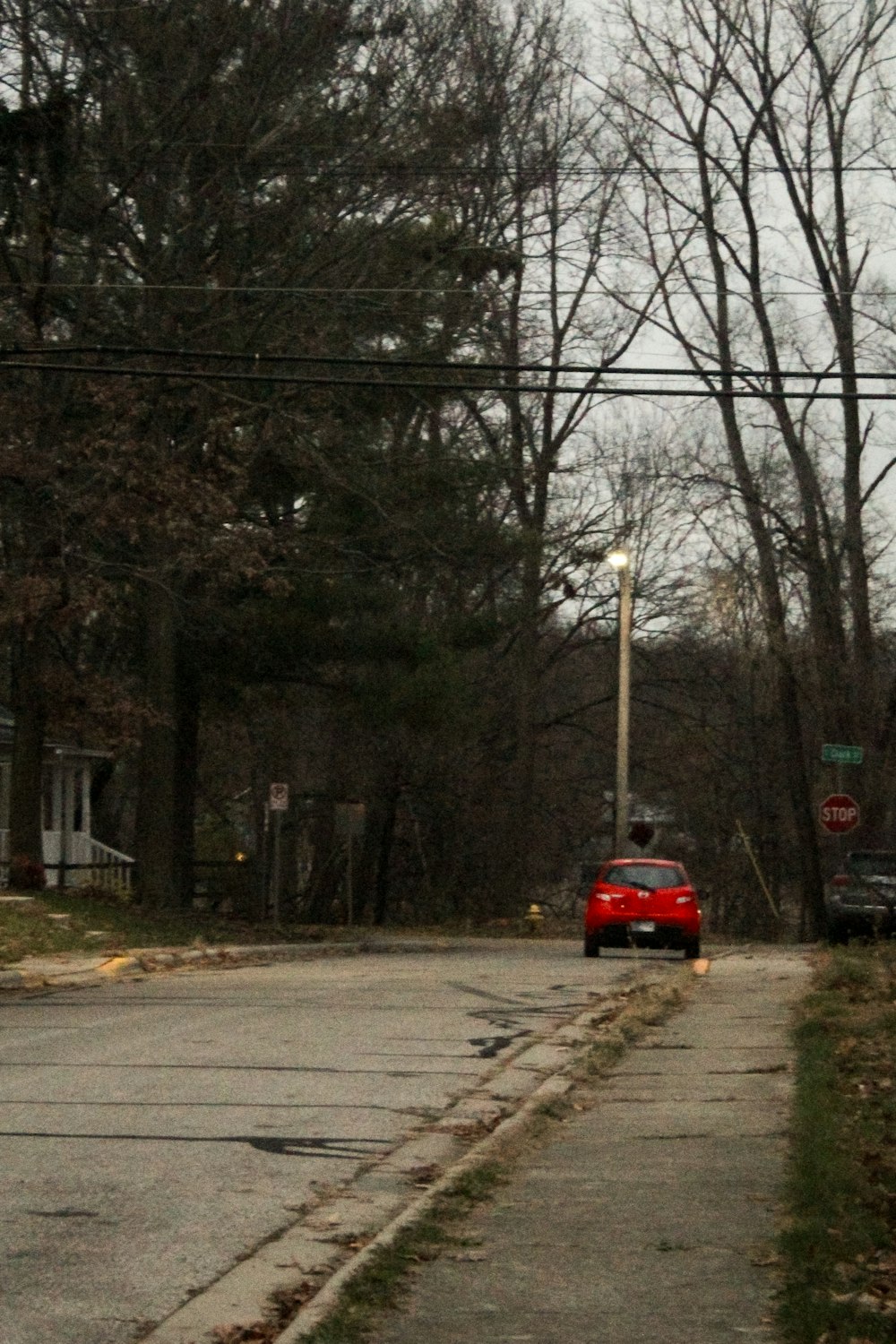 a red car driving down a street next to a forest