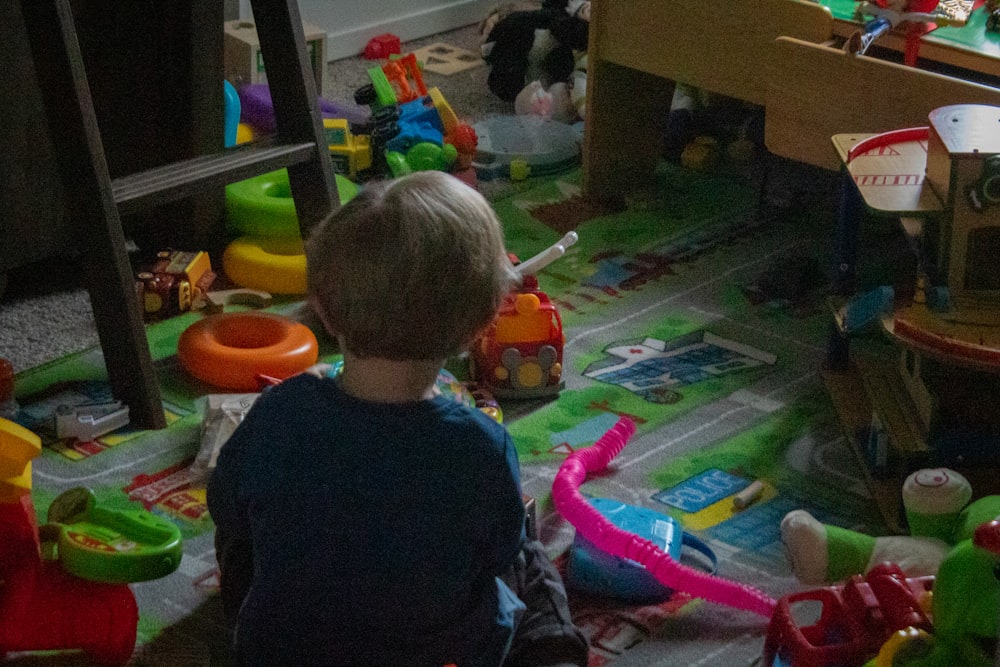 a little boy sitting on the floor in a room full of toys