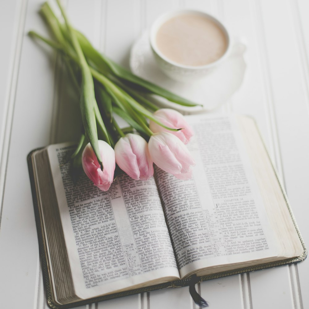 a cup of coffee and some pink tulips on a book