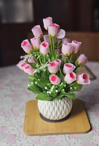 a white vase filled with pink flowers on top of a table
