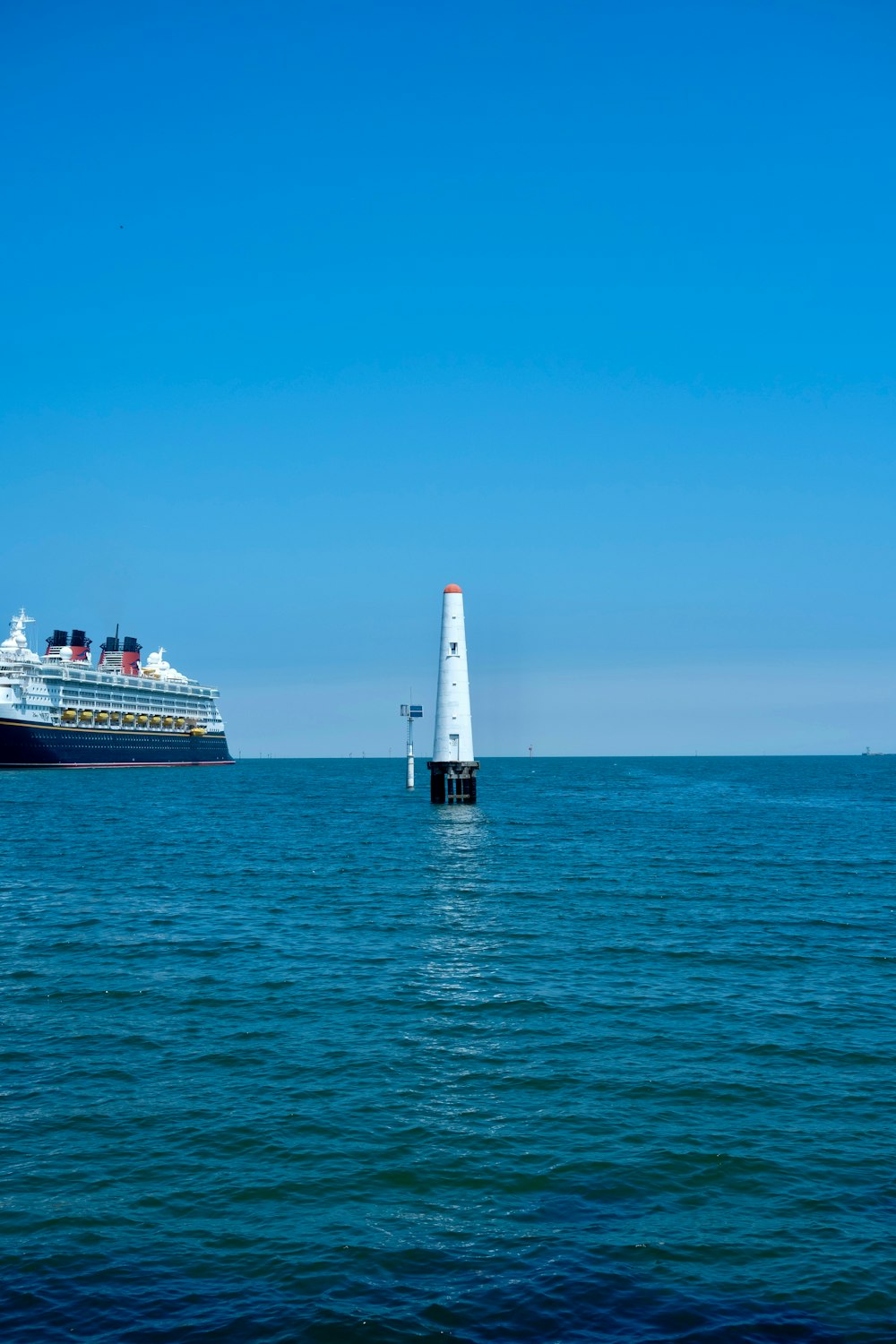 a large cruise ship in the distance with a lighthouse in the foreground