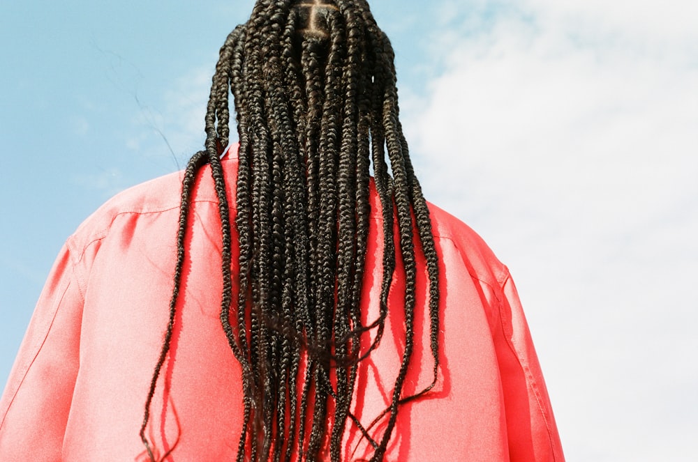 a man with long dreadlocks standing in front of a blue sky