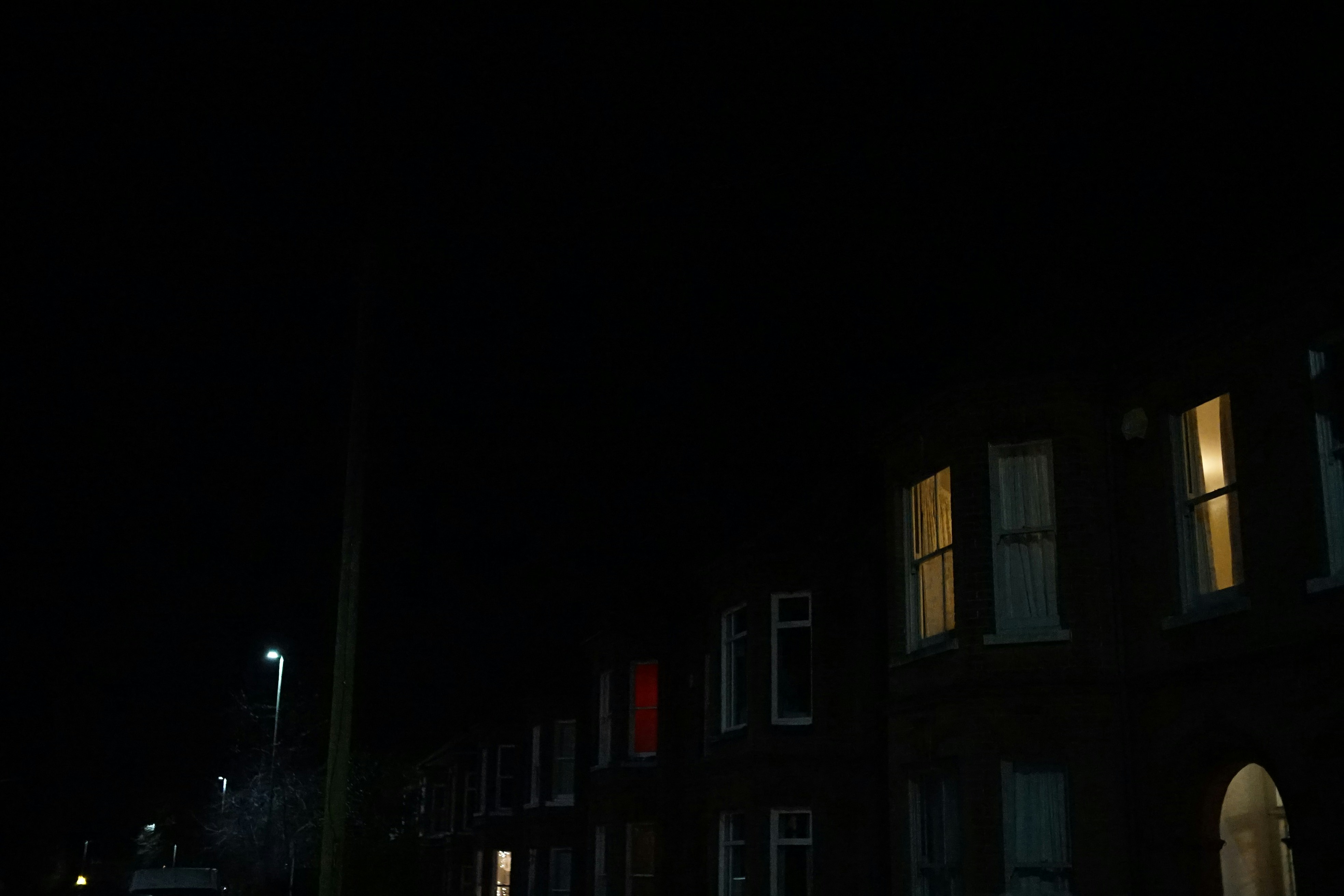 Dark urban street at night with deep shadows, minimal artificial light, architectural moody atmosphere