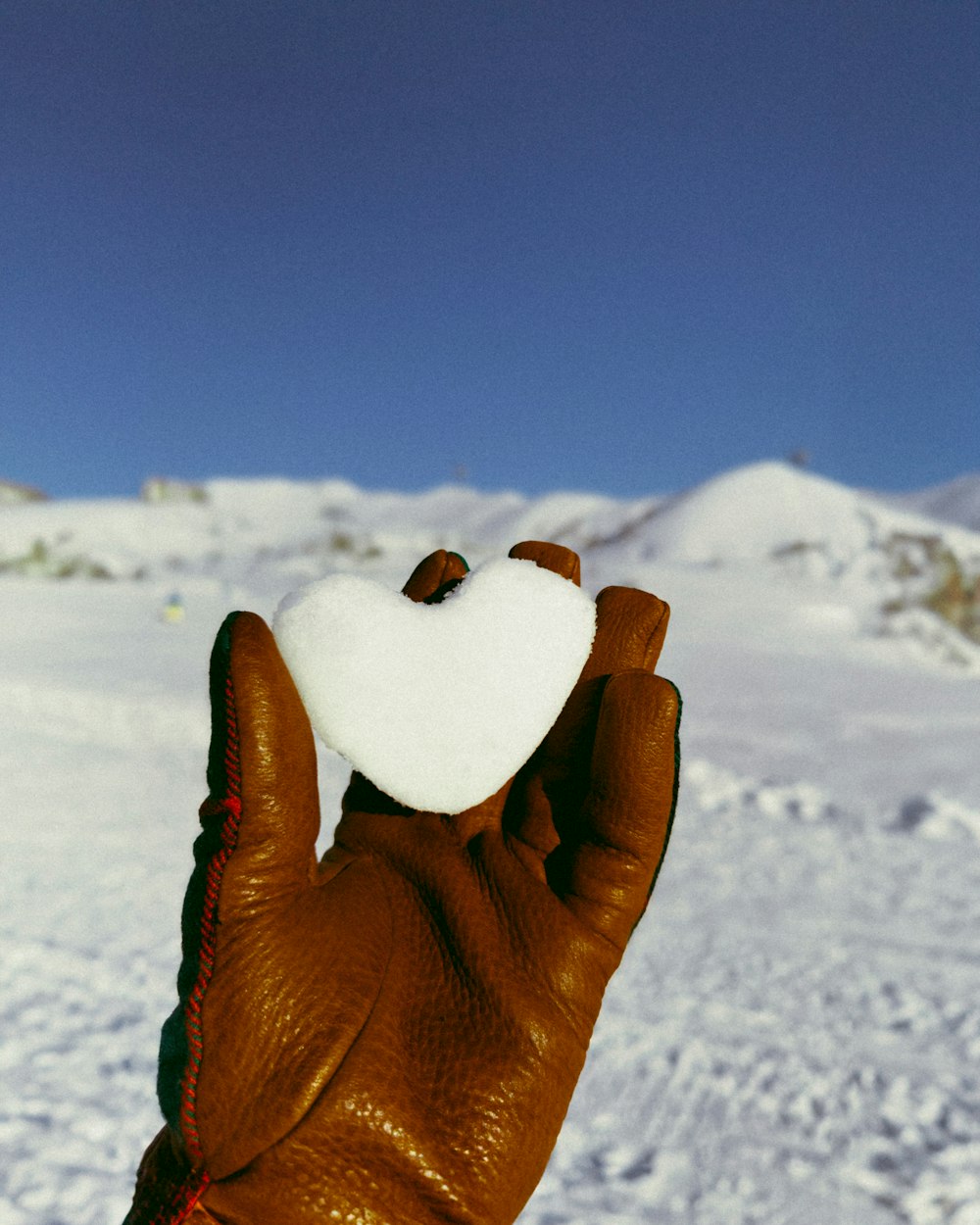 a gloved hand holding a heart shaped object in the snow