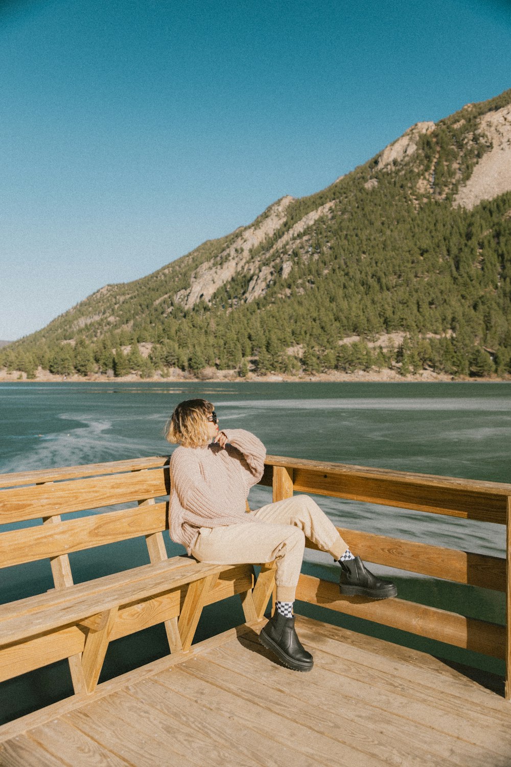 a woman sitting on a wooden bench next to a body of water