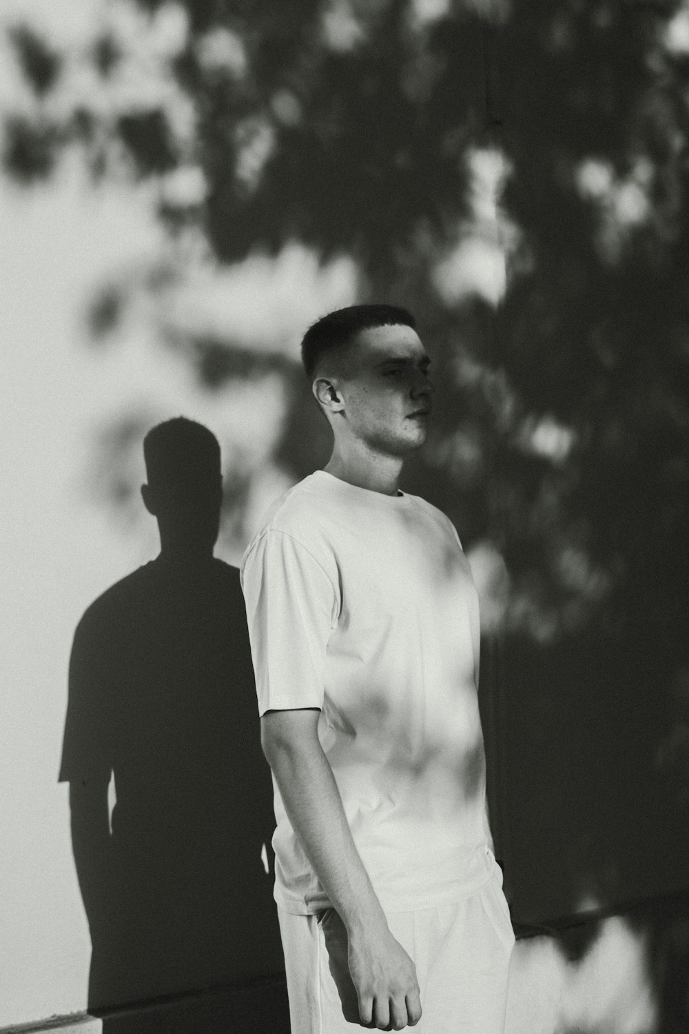 a black and white photo of a man standing next to a tree