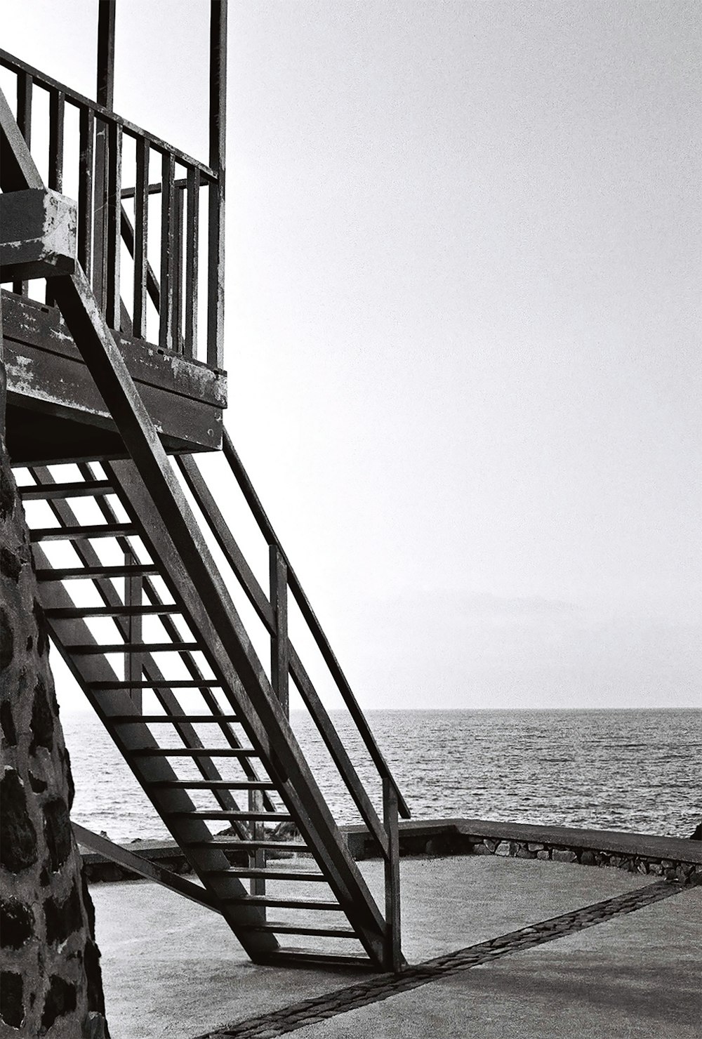 a black and white photo of a staircase next to the ocean