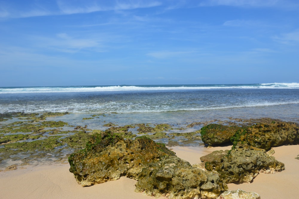 a sandy beach with rocks and a wave coming in