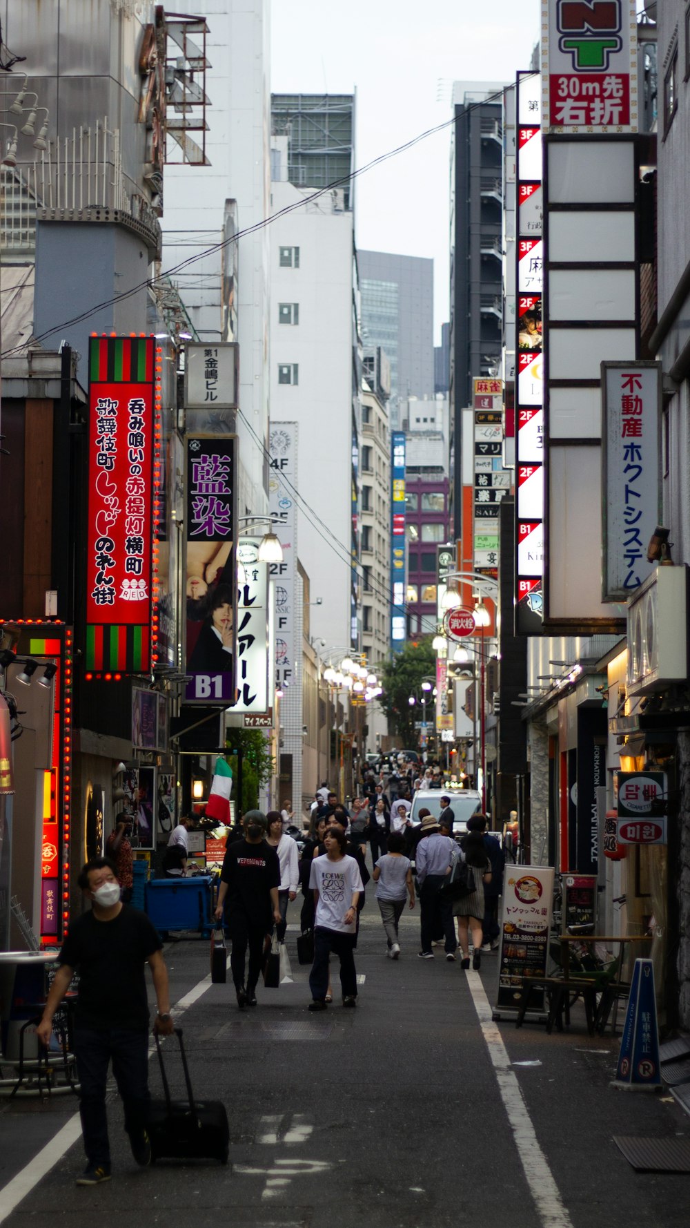 a group of people walking down a street next to tall buildings