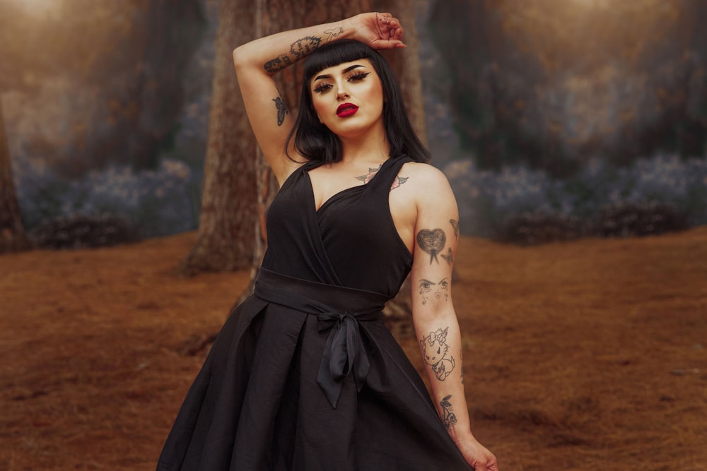 a woman in a black dress with tattoos on her arms