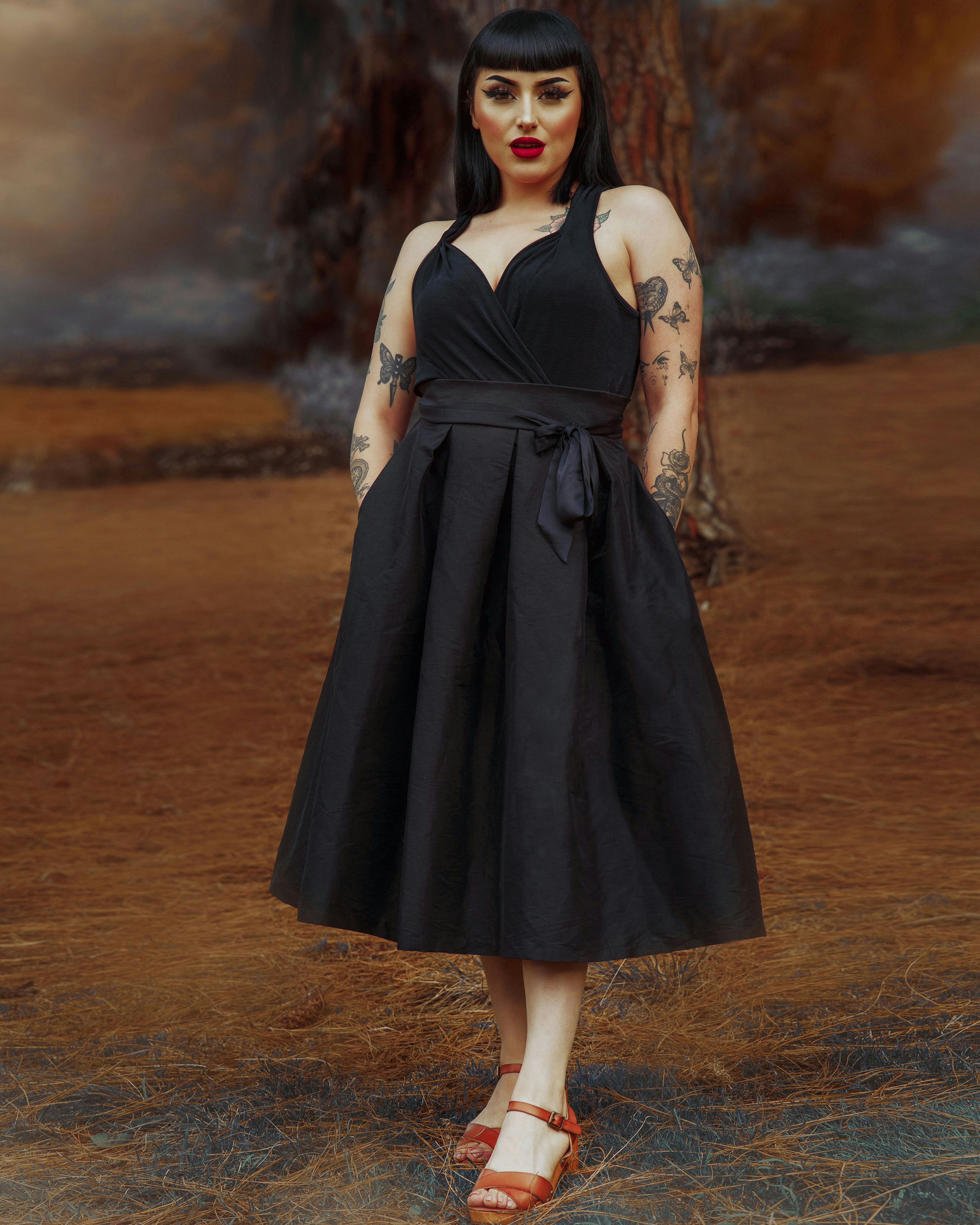 a woman in a black dress standing in front of a tree