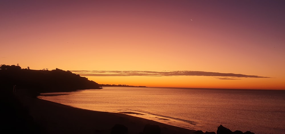 a sunset view of a beach with a hill in the background