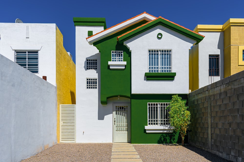 a green and white house sitting next to a white fence