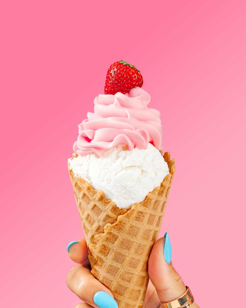 una mano sosteniendo un cono de helado con una fresa encima