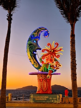 a colorful sculpture on the beach with palm trees