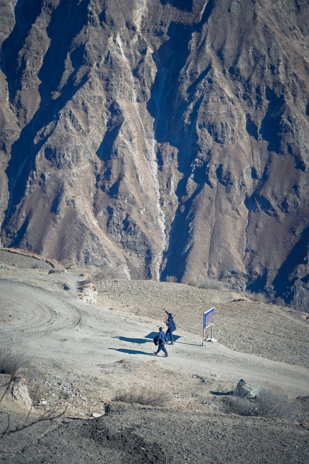two people walking on a dirt road in front of a mountain