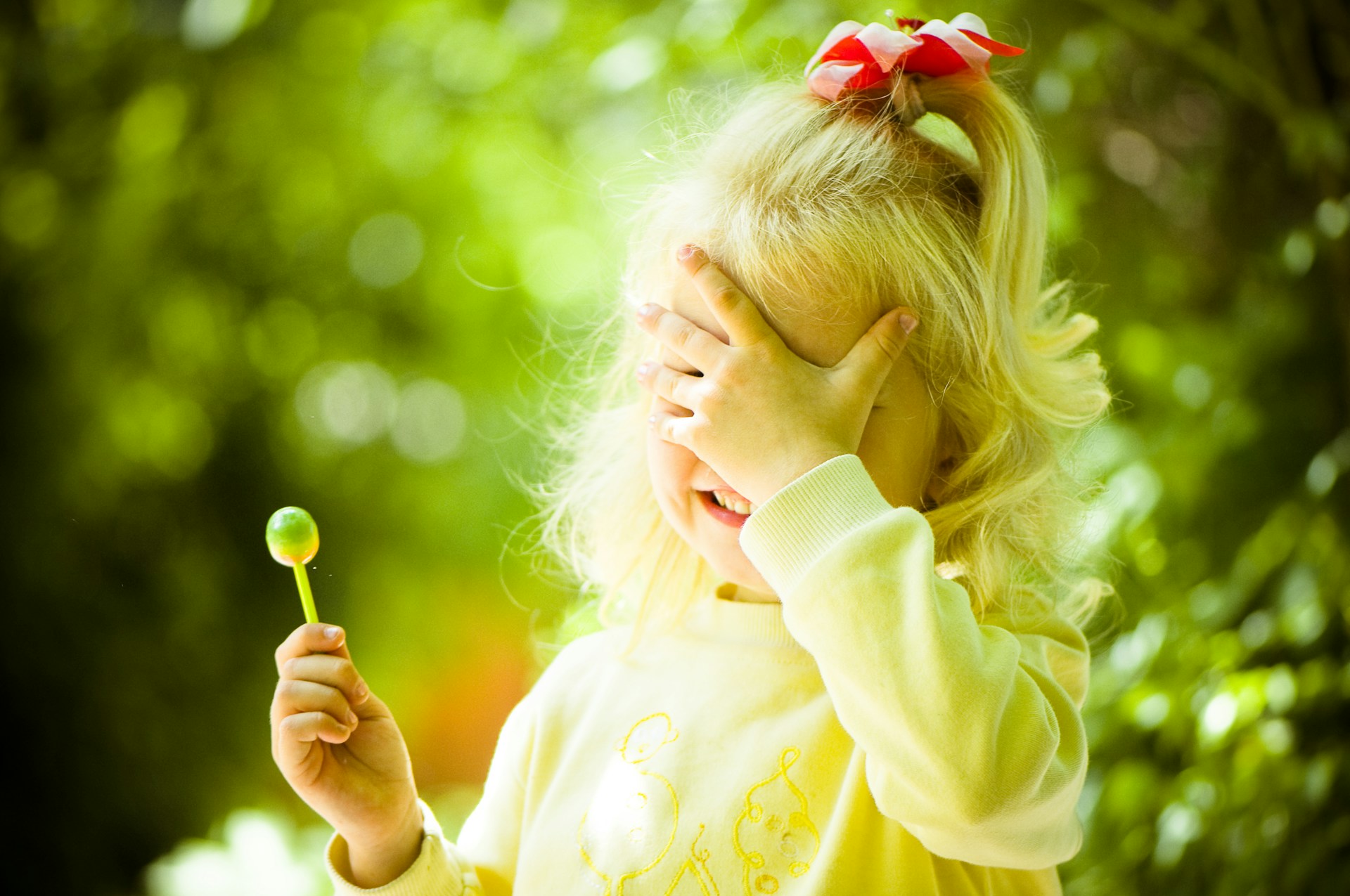 a little girl holding a flower and covering her eyes