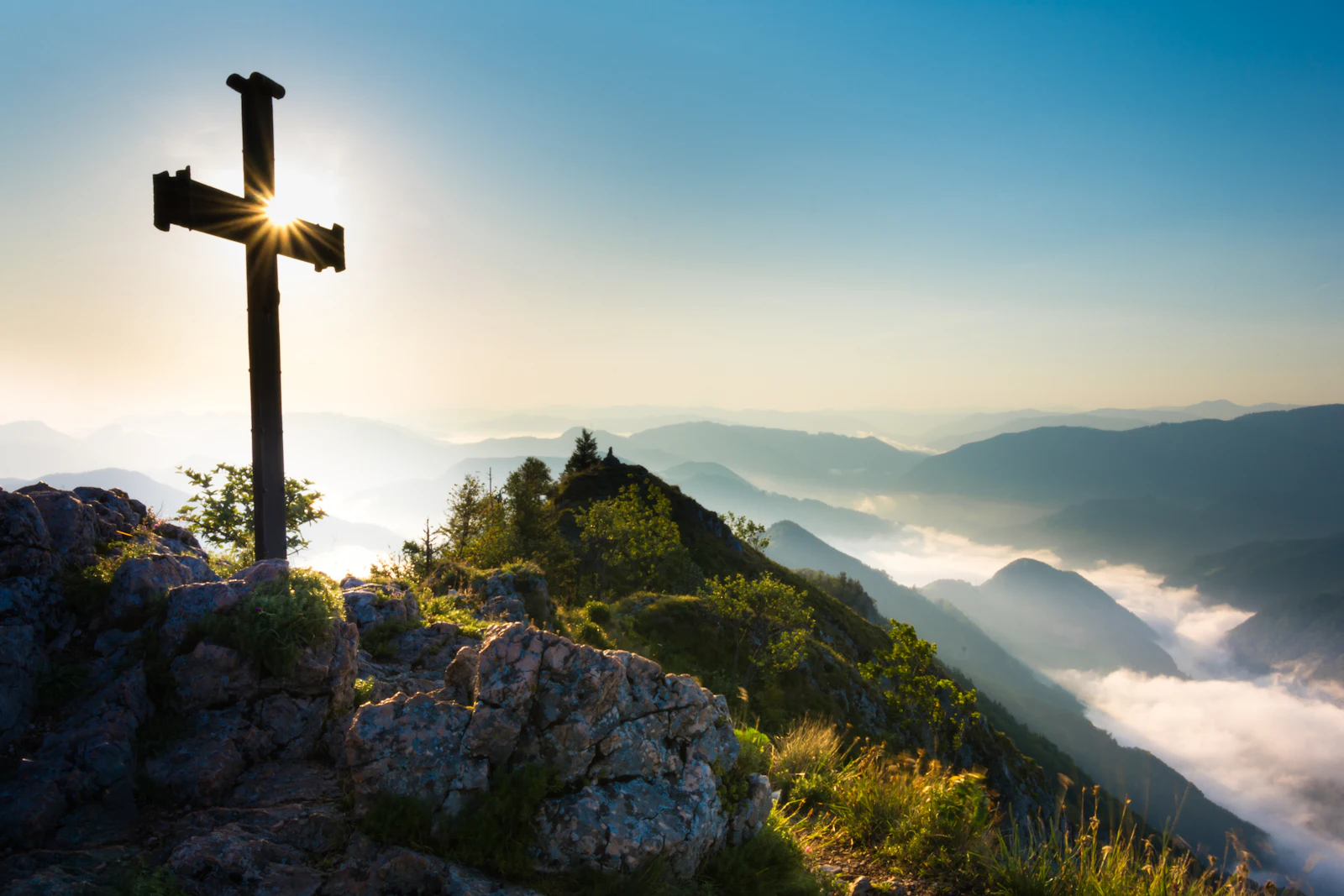 A cross silhouetted on a mountain summit against the sky