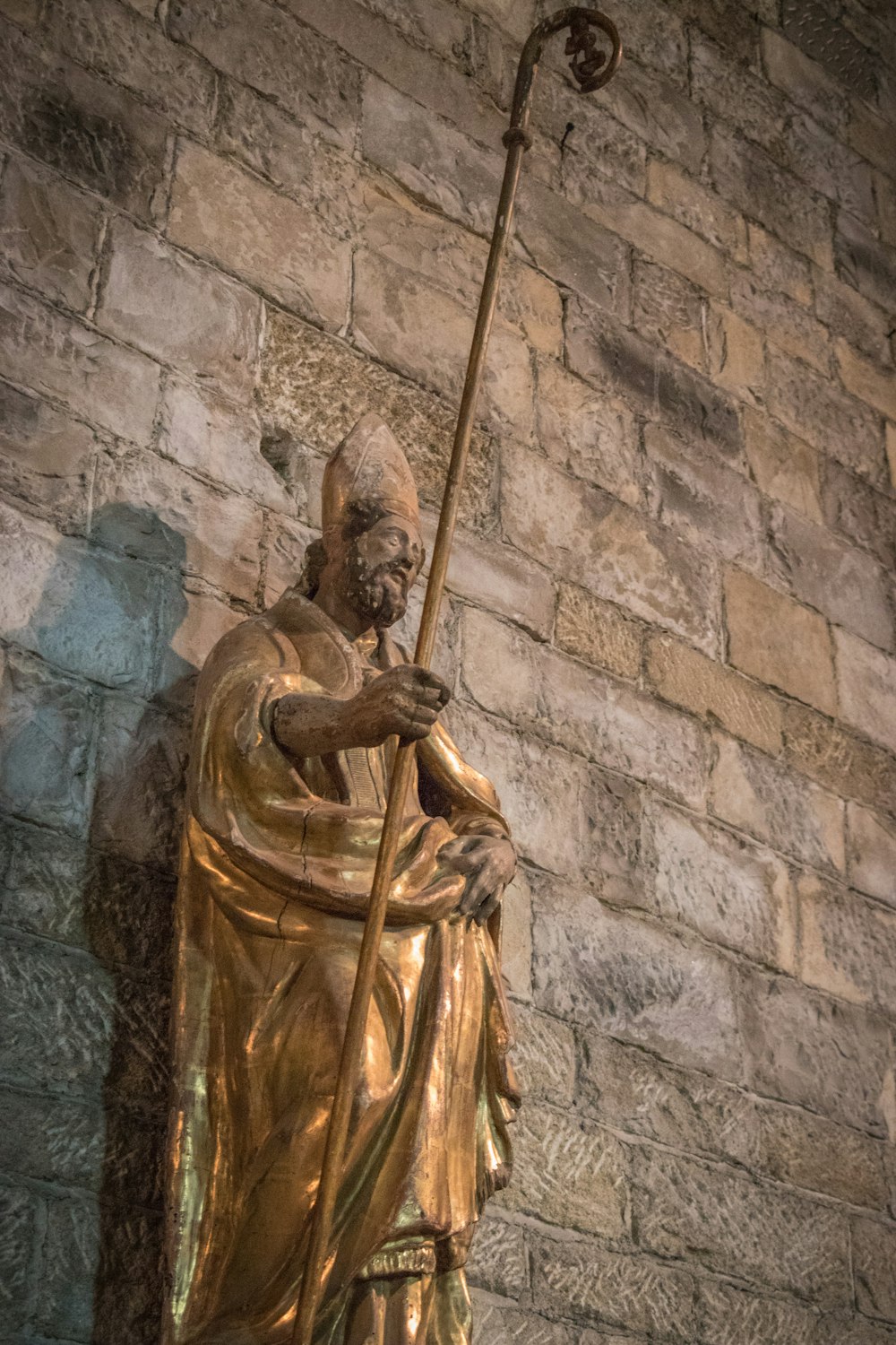 a statue of a man holding a staff in front of a brick wall
