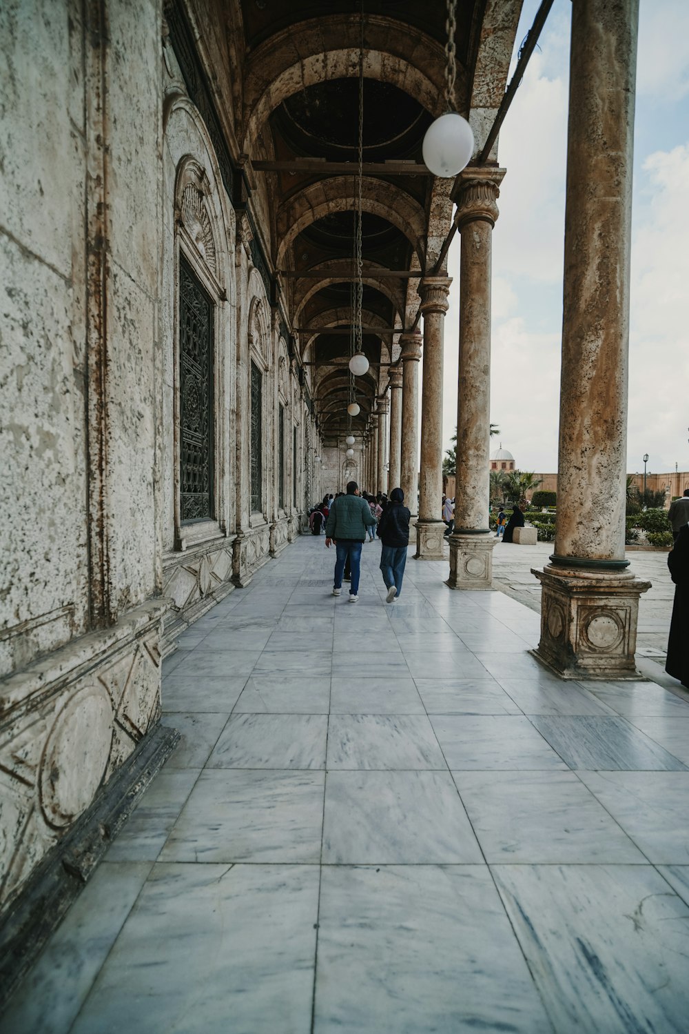 a group of people walking down a sidewalk next to tall pillars