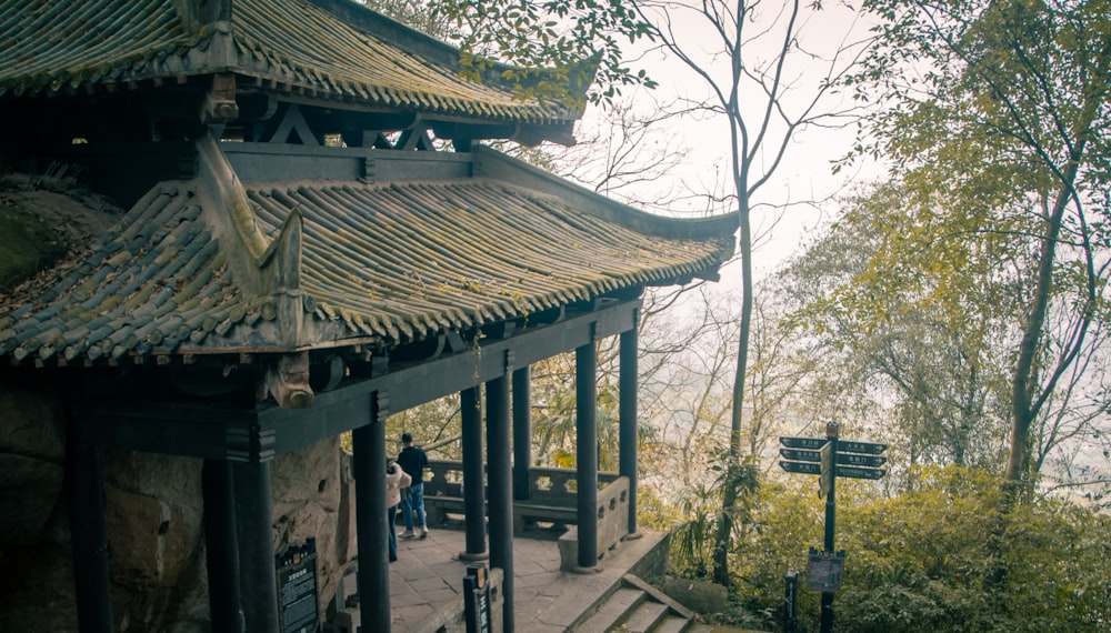 a stone building with a wooden roof next to a forest