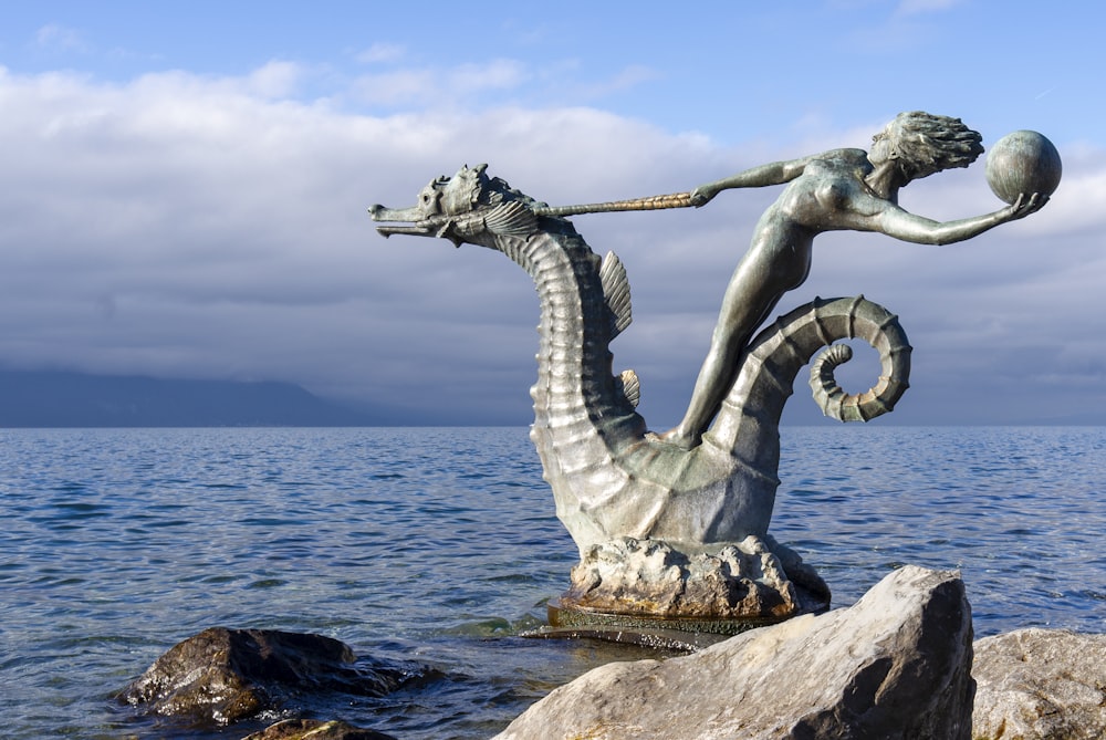 a statue of a woman and a dragon on a rock in the water