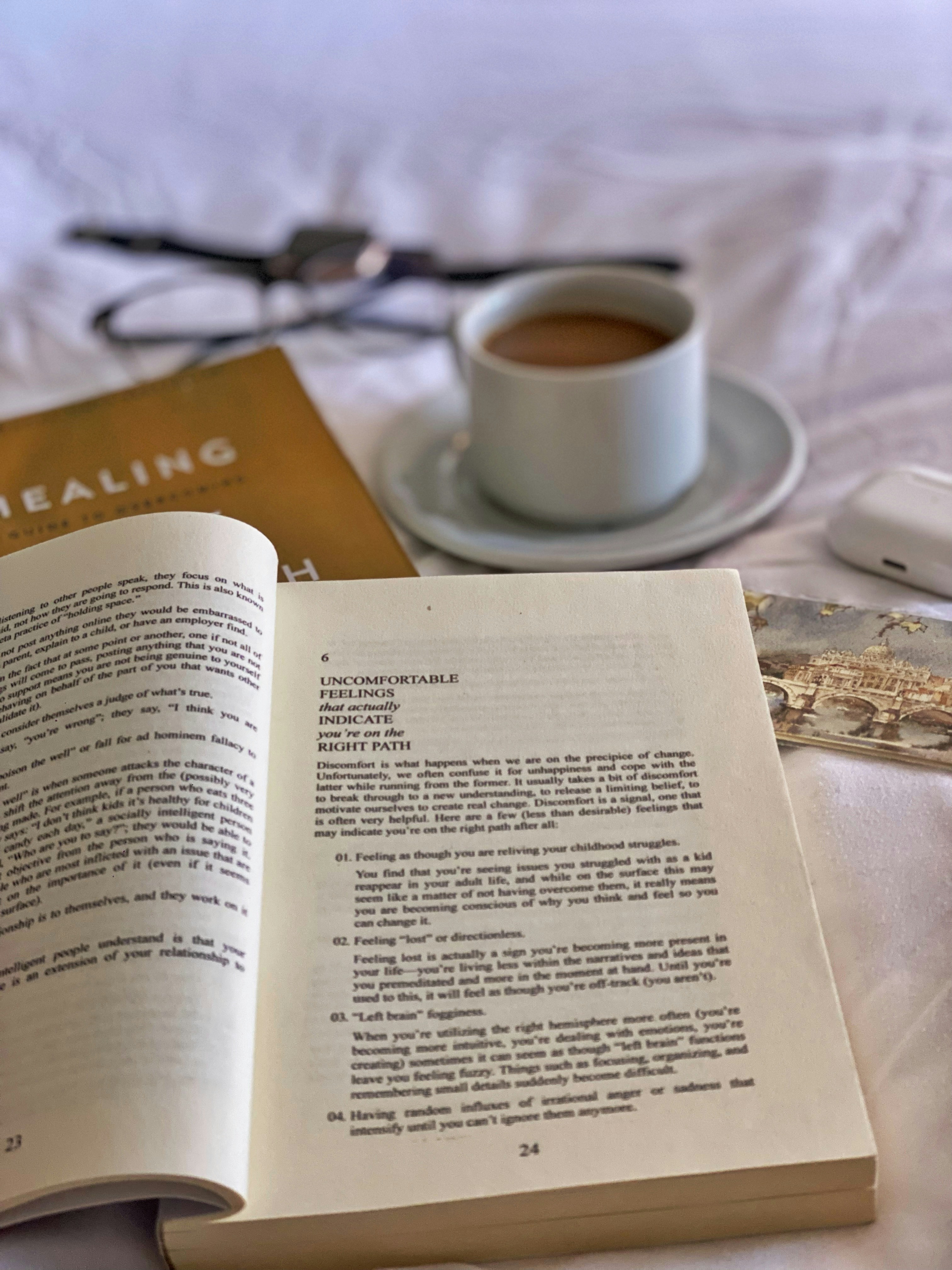 An open book placed on top of a bed next to a cup of coffee.