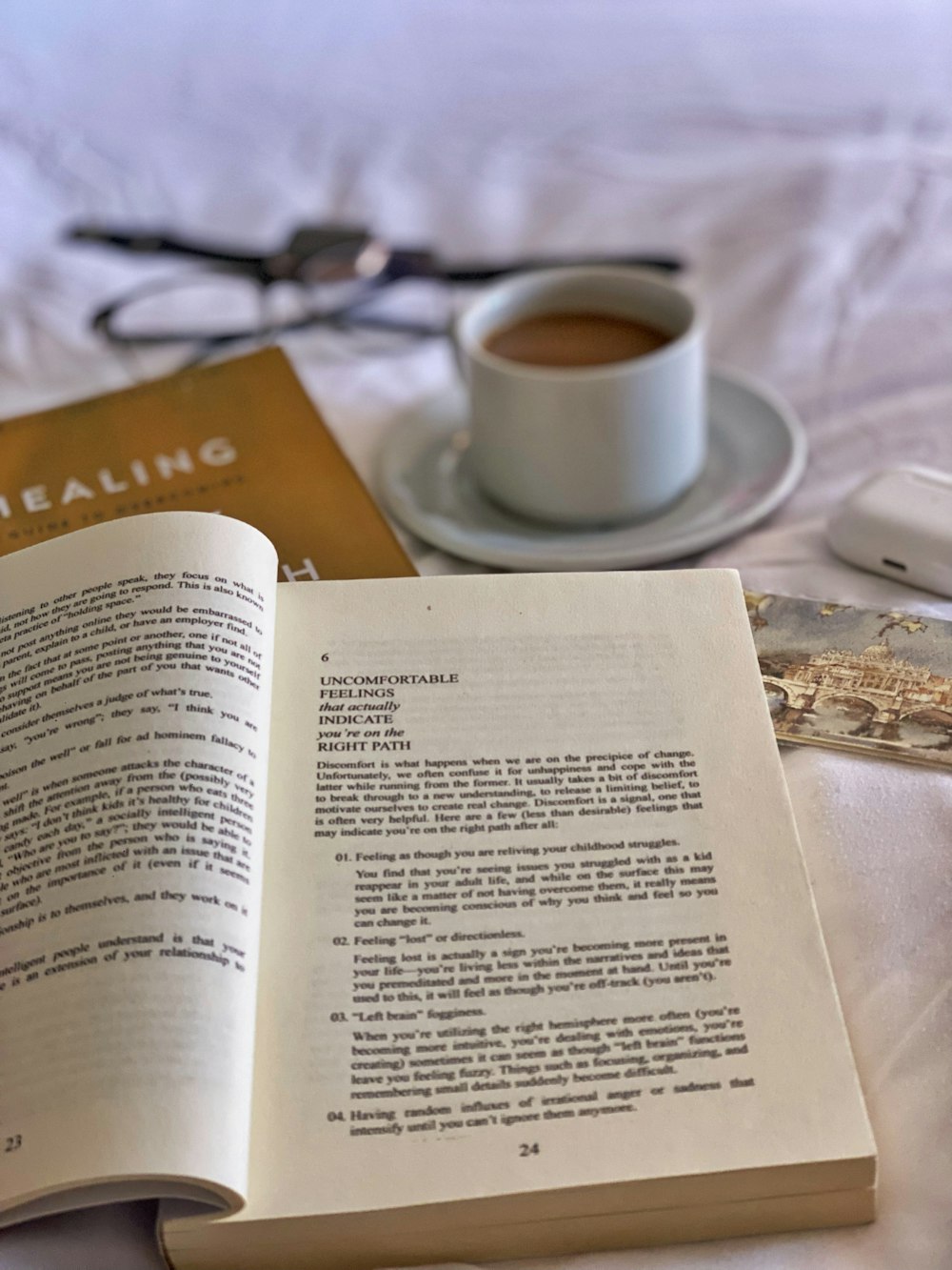 an open book sitting on top of a bed next to a cup of coffee