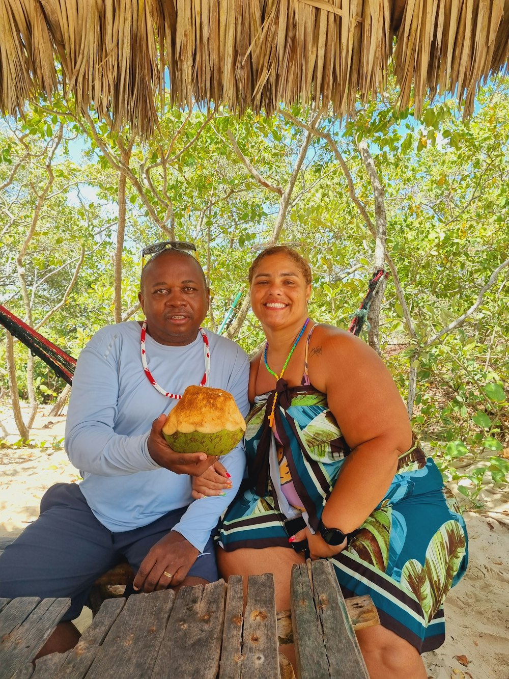 a man and a woman sitting on a bench holding a coconut