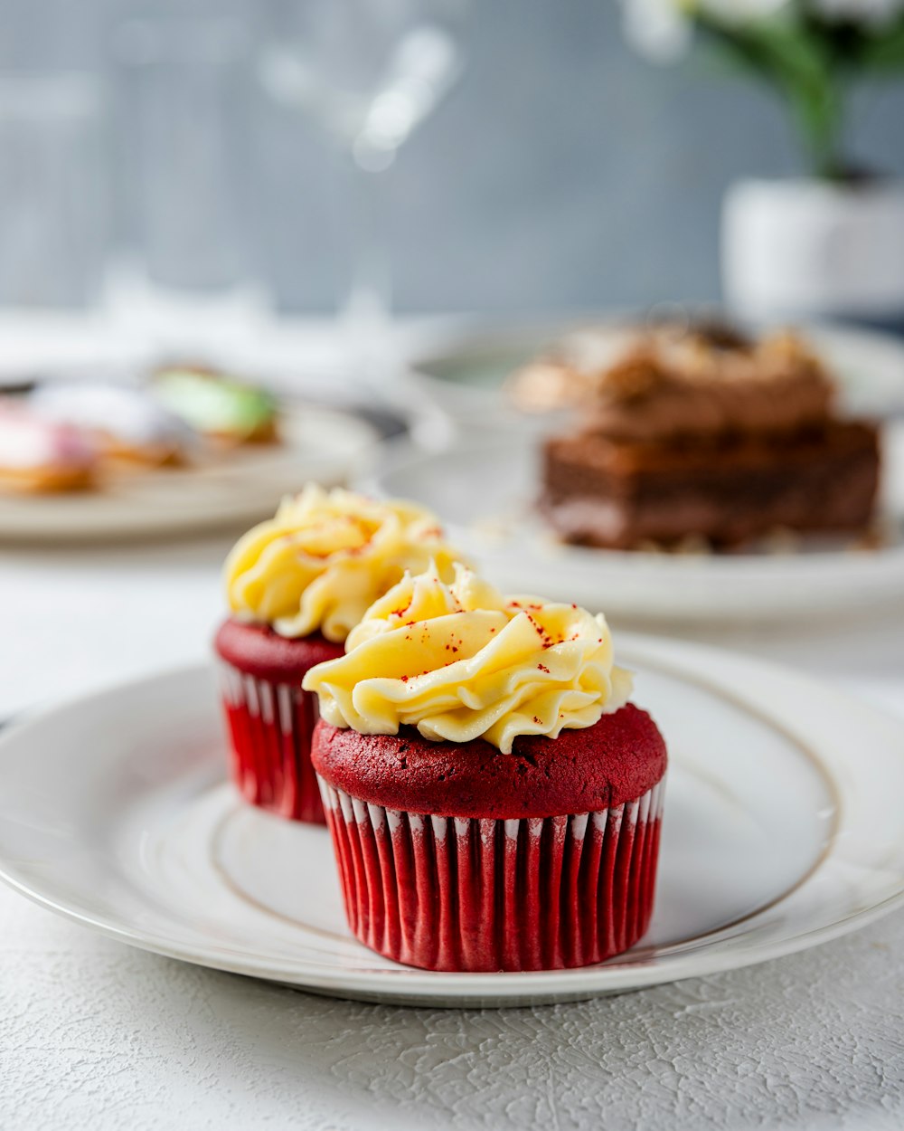 two red cupcakes with white frosting on a plate