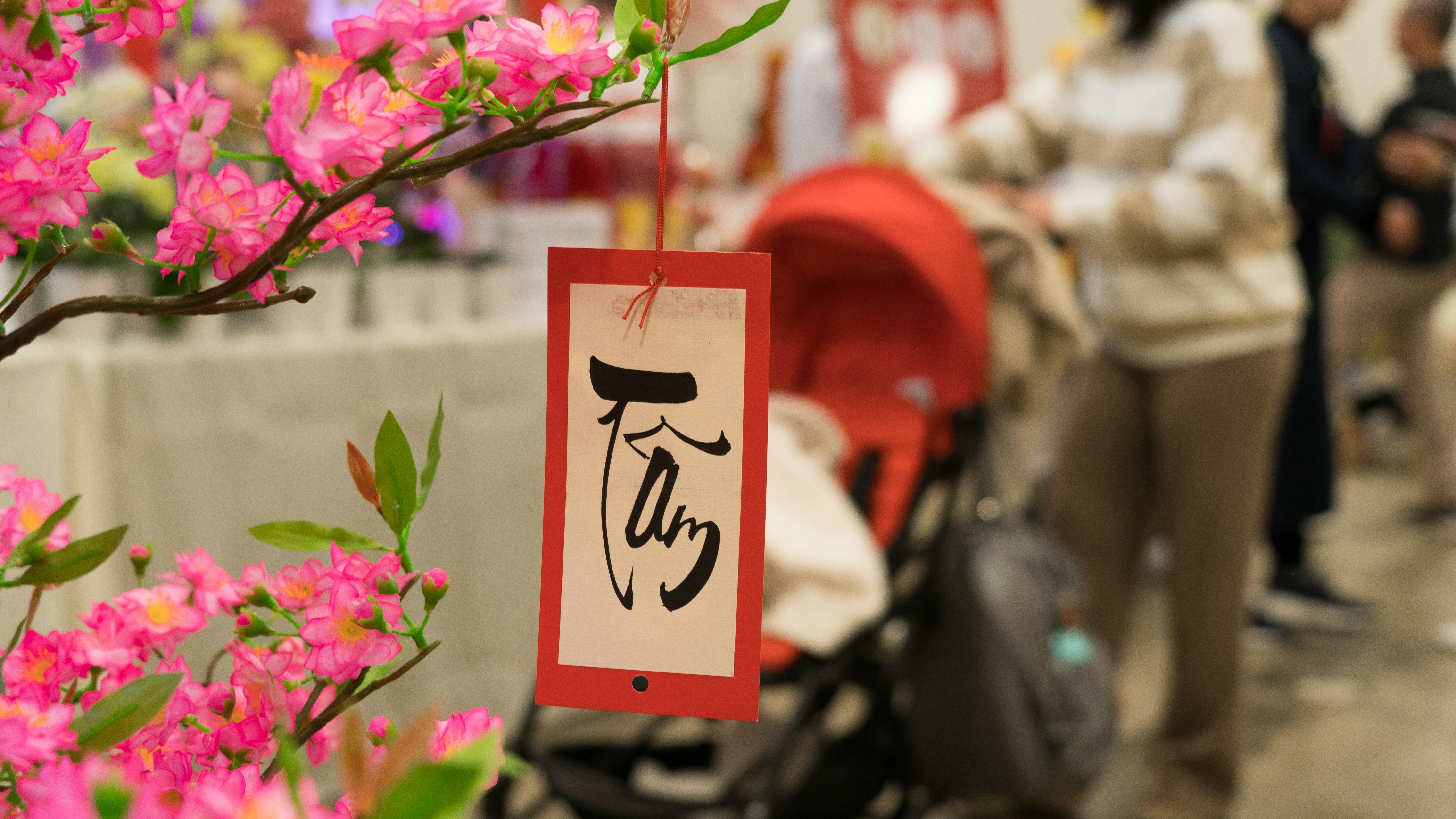 a sign hanging from a tree with pink flowers, "Heart" Calligraphy is hanging on an artificial blossom tree in New Year Festival.