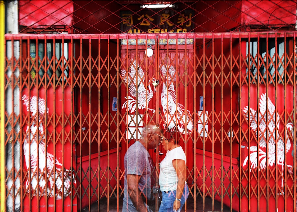 a man and a woman standing in front of a red fence