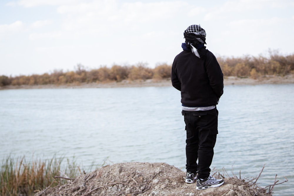 a man standing on top of a rock next to a body of water