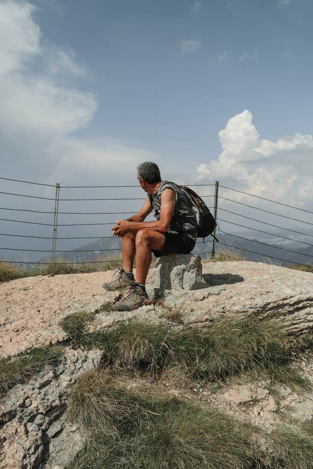 a man sitting on top of a rock near a fence