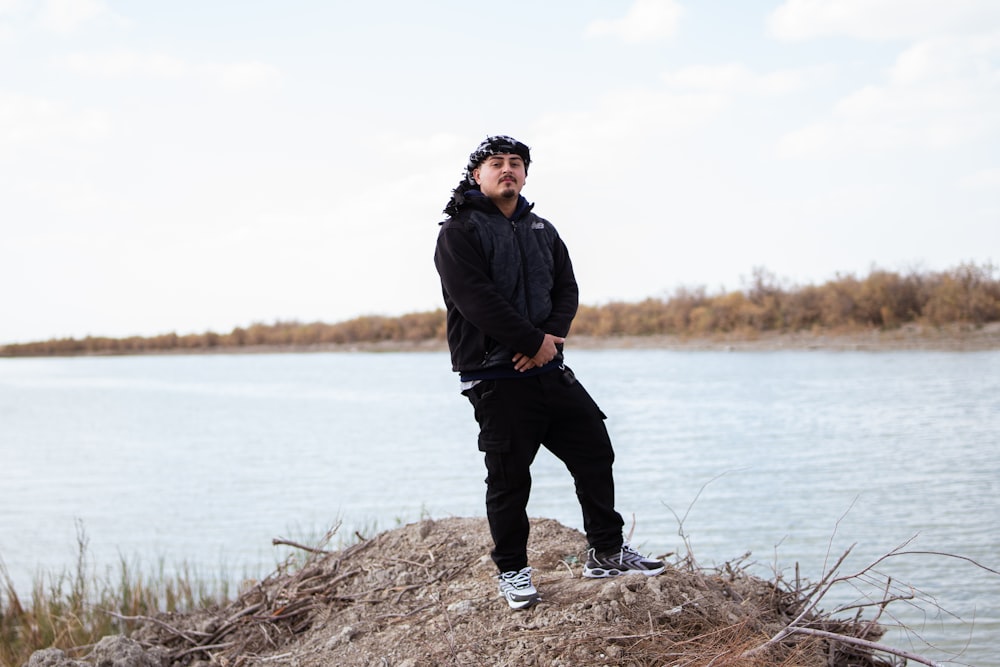 a man standing on top of a rock next to a body of water