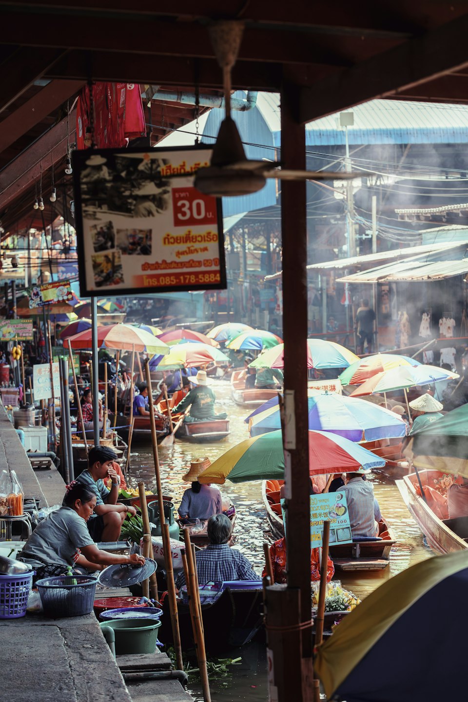 Vendors under umbrellas selling produce from wooden boats at a Thai floating market