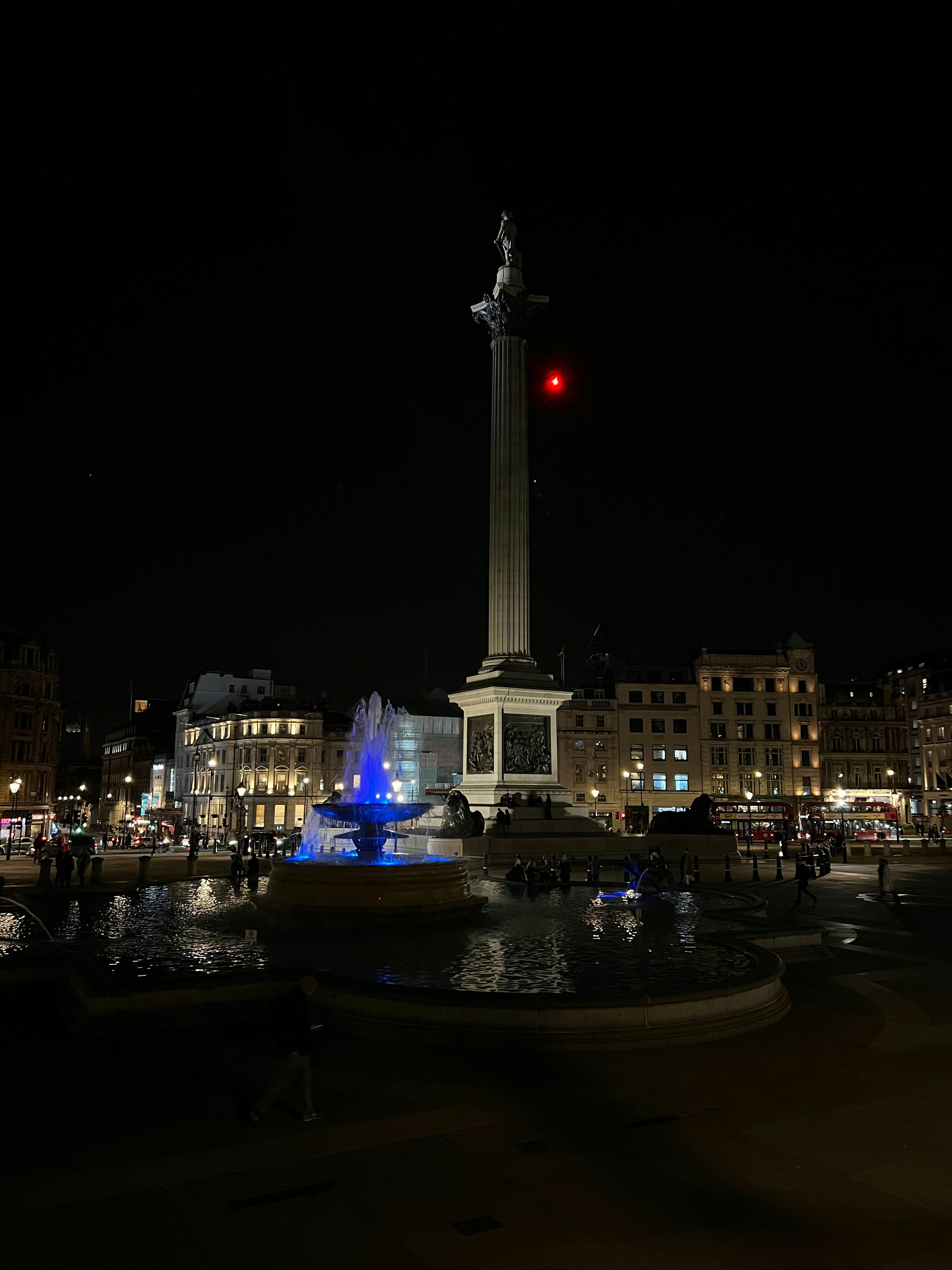 a red light shines in the night sky over a fountain