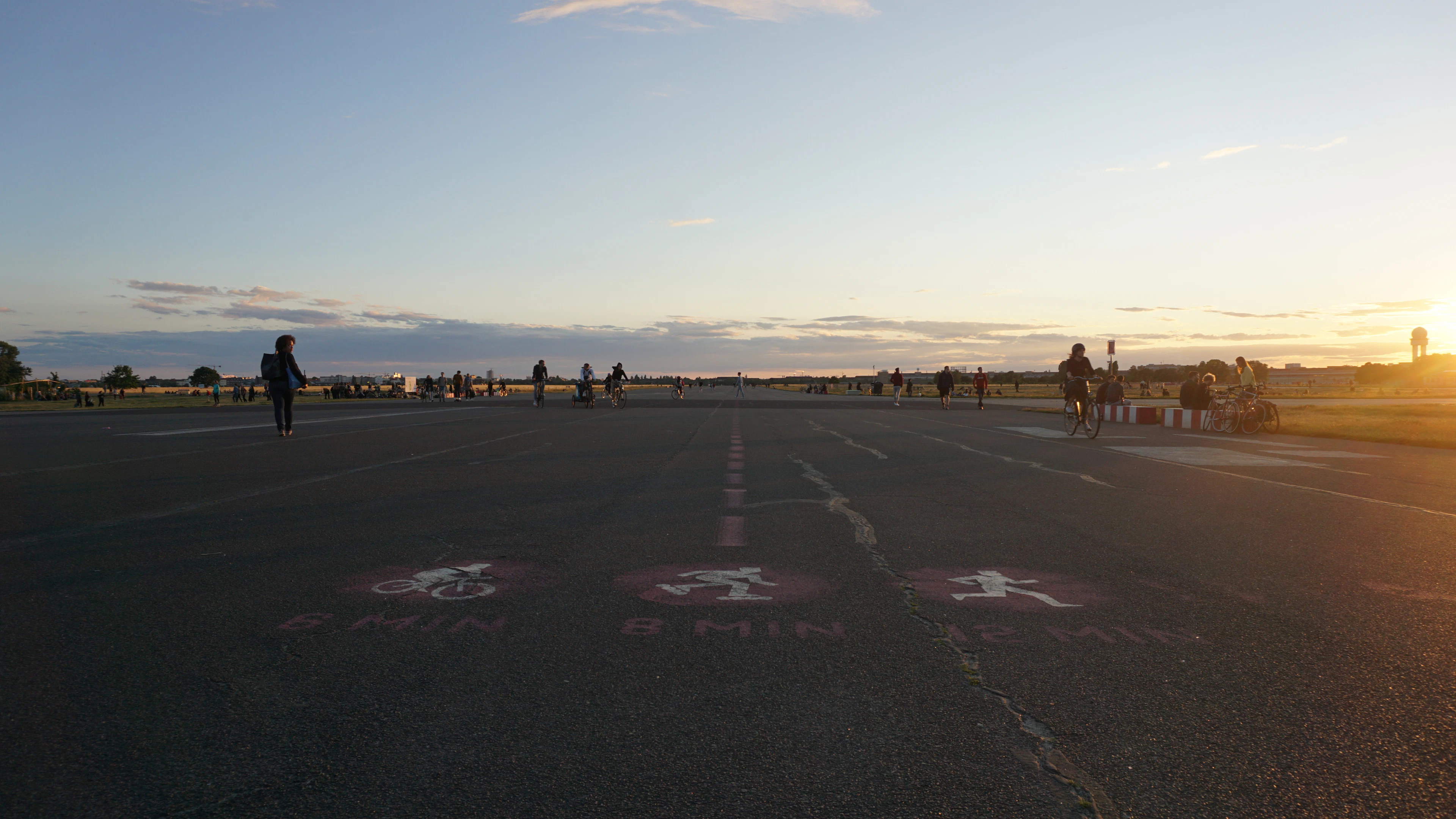 Cyclists and walkers cross the old Tempelhofer Feld runway at sunset, its faded markings still on the tarmac.