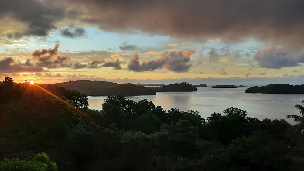 the sun is setting over a lake surrounded by trees