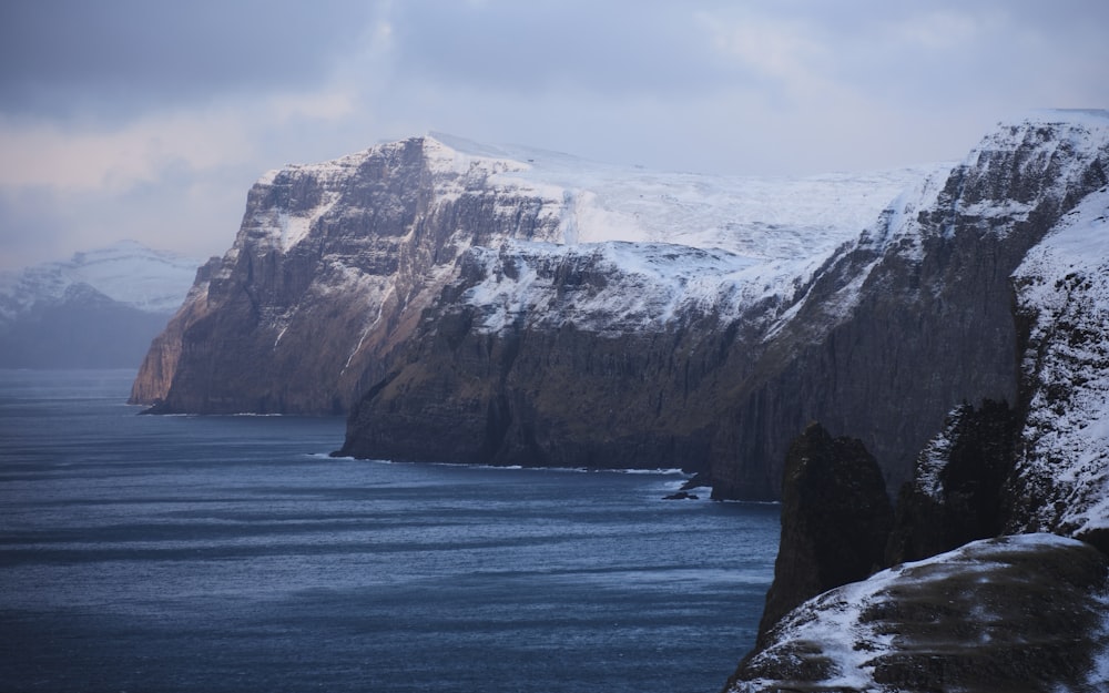 a snowy mountain with a body of water in the foreground