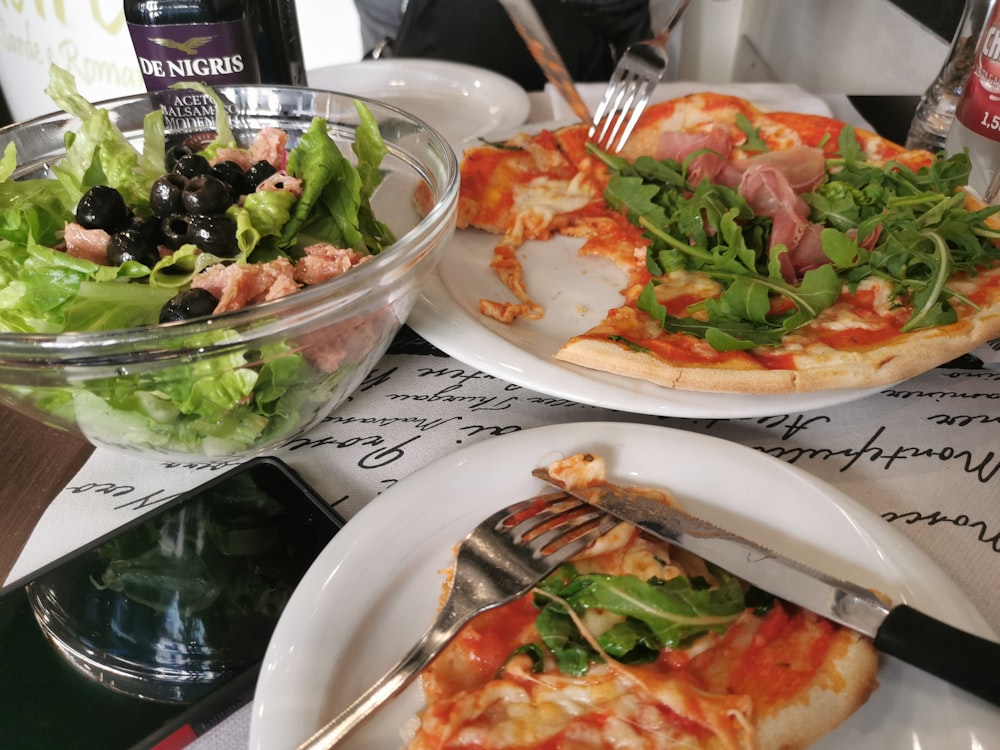 a table topped with plates of pizza and salad