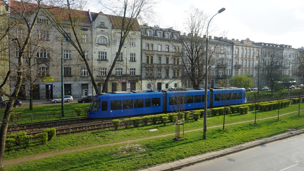 a blue train traveling down train tracks next to a lush green park
