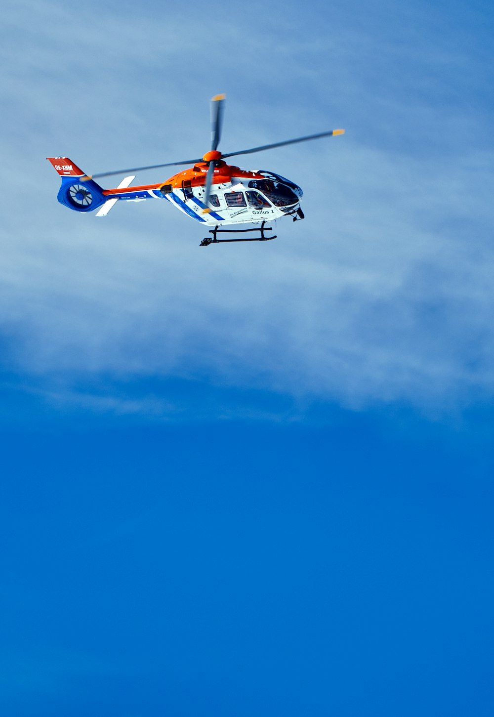 a helicopter flying through a blue sky with clouds