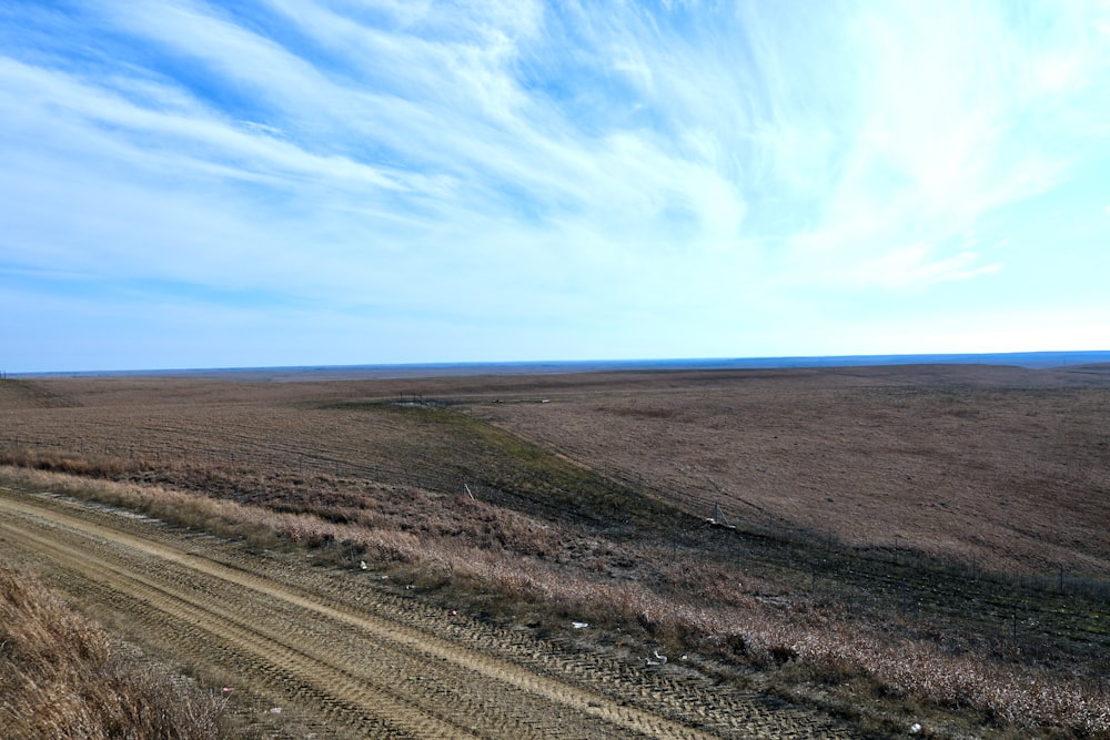 a dirt road running through a dry grass field