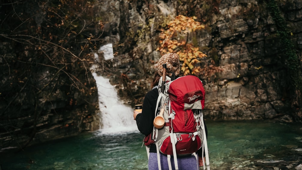 a person with a backpack standing in front of a waterfall