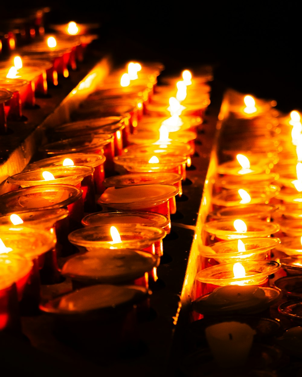 many lit candles are lined up in rows